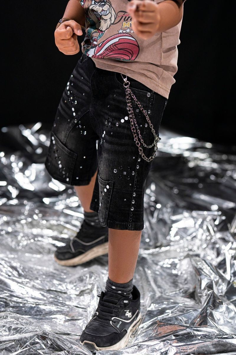 On Time Fashions black distressed denim shorts for kids with white paint splatters and silver stud details, featuring a detachable chain.