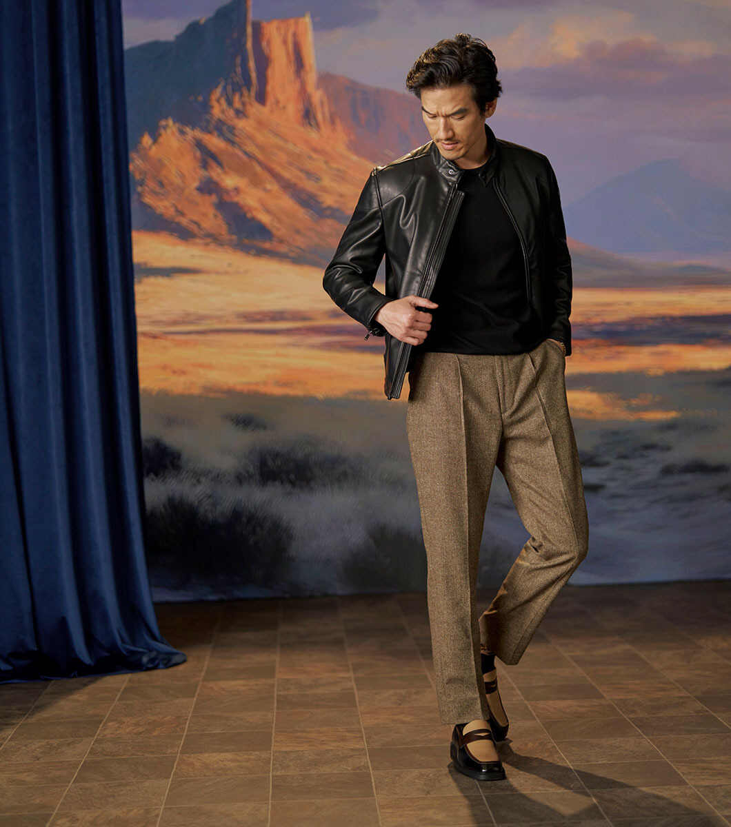 Model wearing Stacy Adams Everett Black/Brown loafers with tan trousers and a dark jacket against a desert stage backdrop.