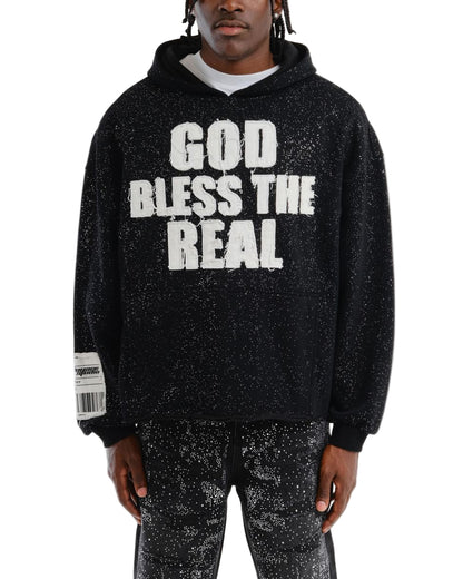 Person wearing a black hoodie with 'GOD BLESS THE REAL' text on a white background