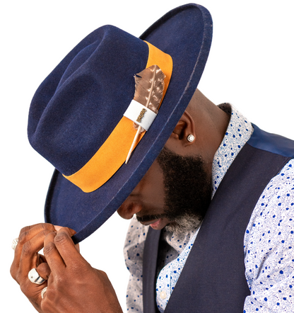 Man wearing a navy blue hat with an orange band and feather, white shirt with blue pattern, and dark vest.