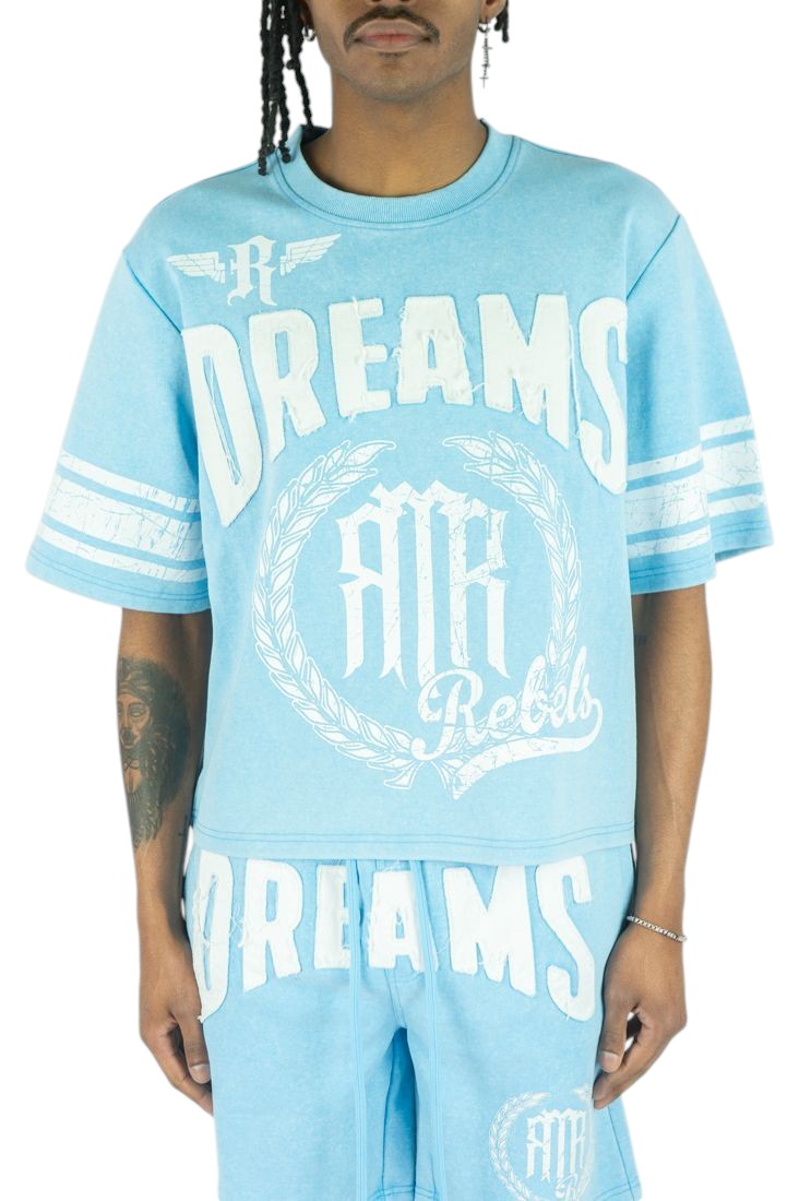 On Time Fashions light blue distressed cotton jersey with white 'Dreams' and 'Rebels' patches and striped sleeves.
