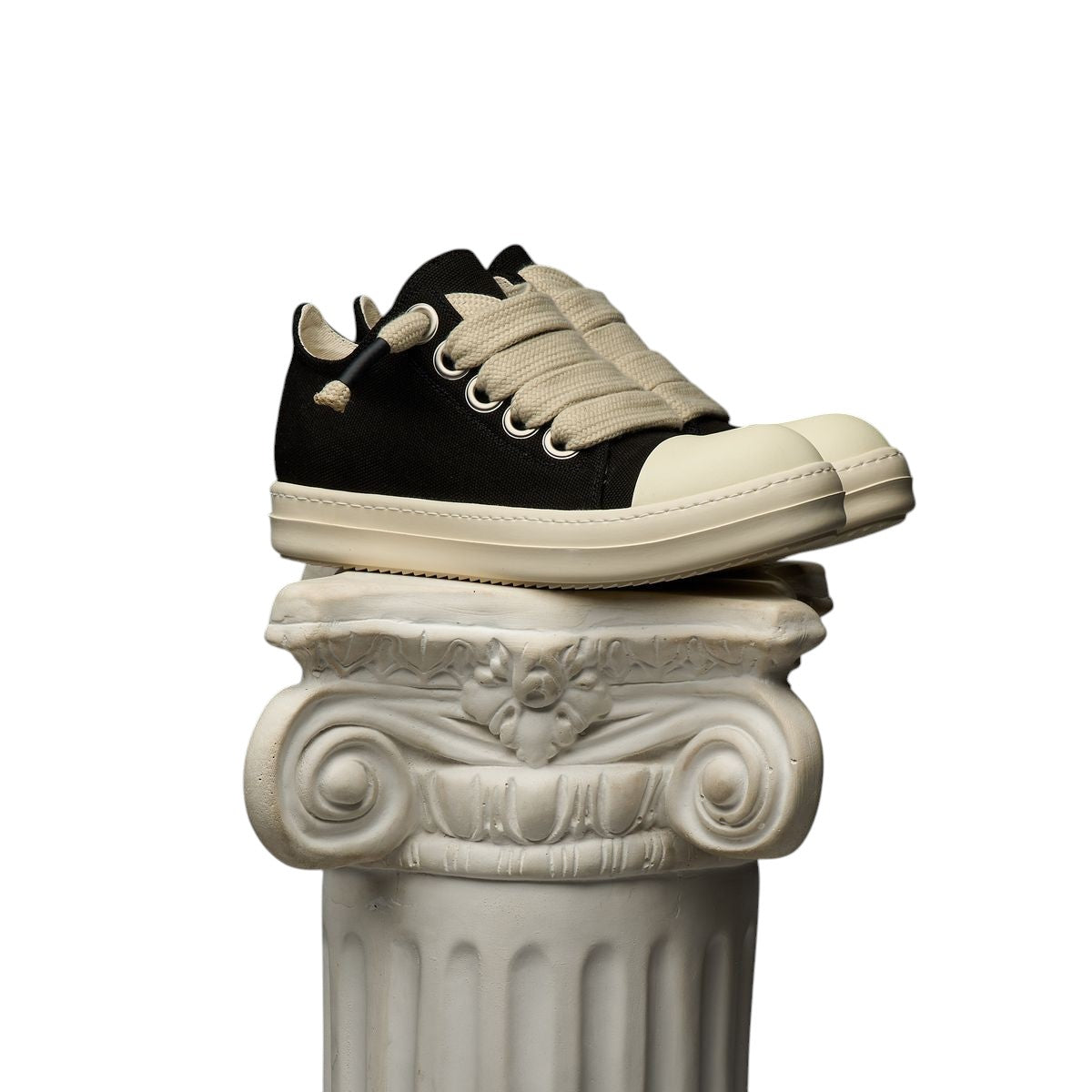 On Time Fashions Duaa Salm 28 black canvas lowtop sneaker with thick cream laces on a decorative stone pillar