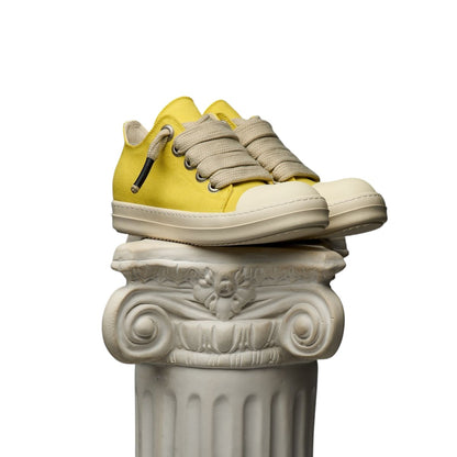 On Time Fashions Duaa Salm 28 yellow canvas lowtop sneakers with thick beige laces resting on a classical stone pillar