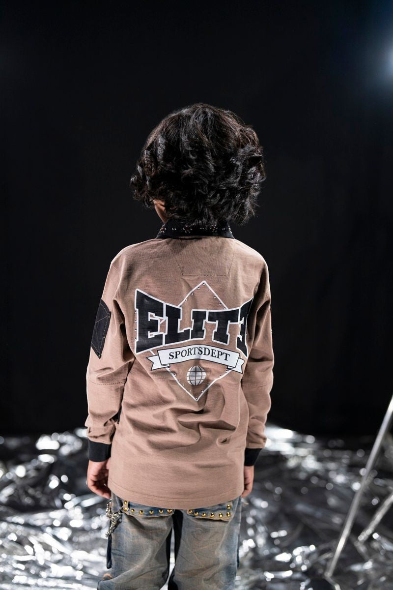 On Time Fashions kid's brown long-sleeve polo with oversized fit, featuring 'Elite Sportsdept' graphic with globe detail and studded collar.