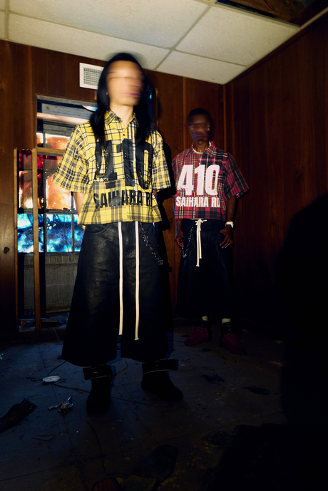 Two models wearing Syair Saihara in a wood-paneled room, captured in blurred motion.