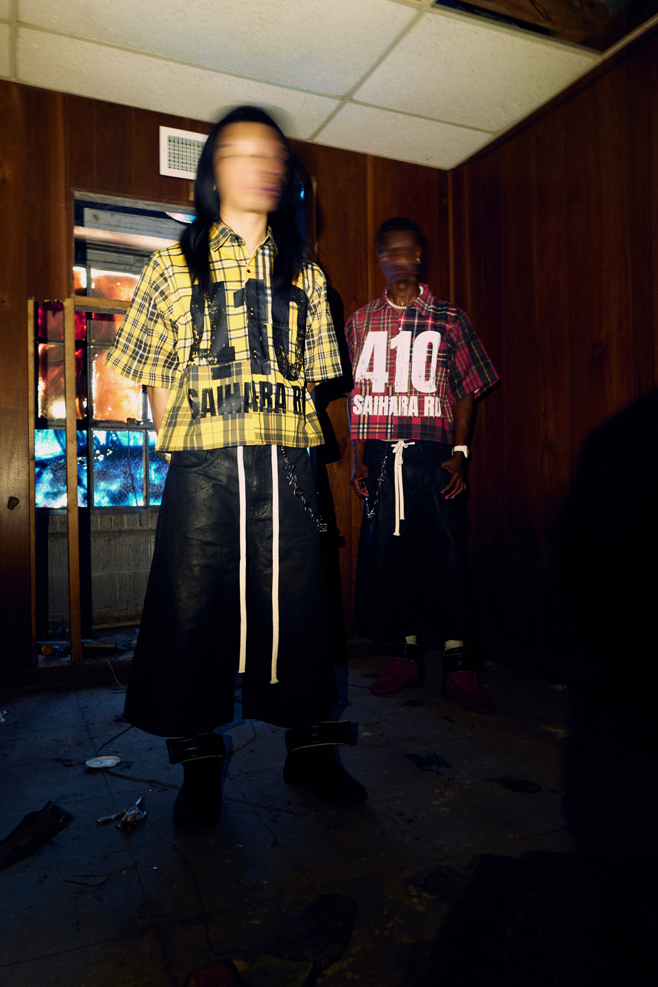 Two models wearing Syair Saihara in a wood-paneled room, captured in blurred motion.
